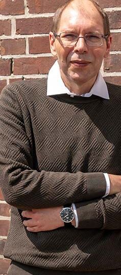 Der erfolgreiche Umschüler André Pardun steht mit verschränkten Armen vor einer geziegelten Hauswand.