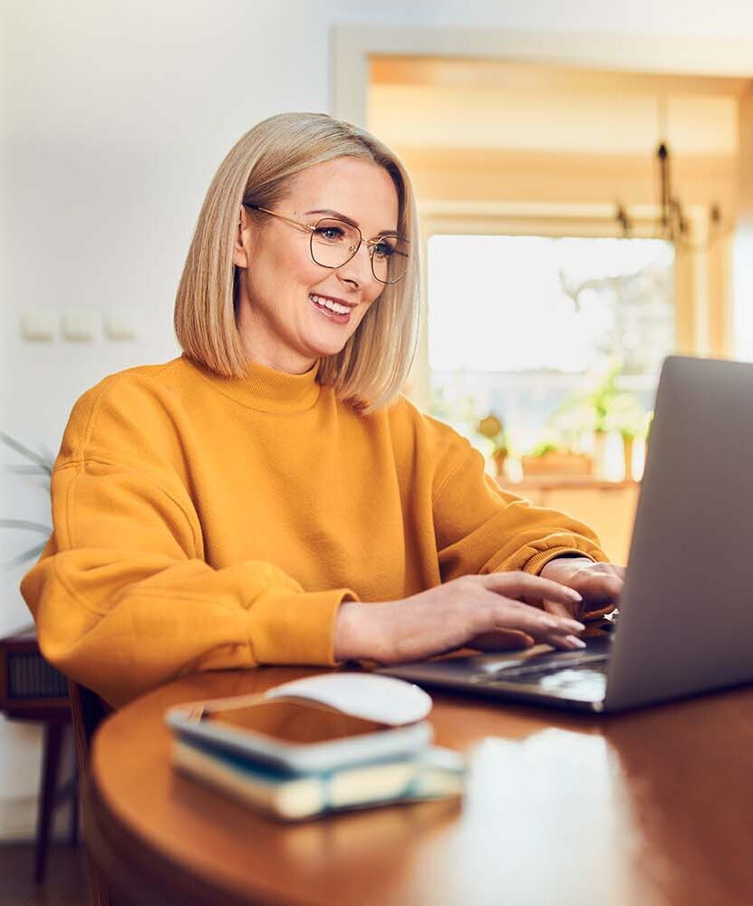 eine Frau sitzt an einem Tisch mit einem Laptop vor orangenem Hintergrund