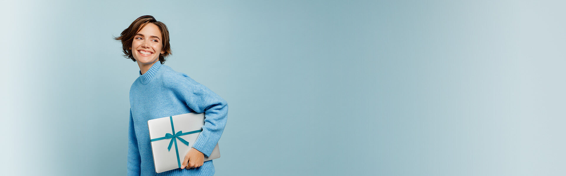 Junge Frau hält einen Laptop mit einer Schleife drum in der Hand und schaut fröhlich